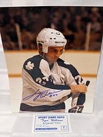 Signed 8x10 color photo of Dave 'Tiger' Williams wearing white and blue Toronto Maple Leafs uniform and helmet, holding hockey stick.