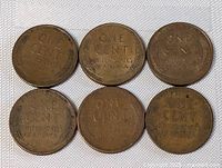 Six early USA one cent coins showing wheat ears reverse, arranged in two rows of three, on white cloth.