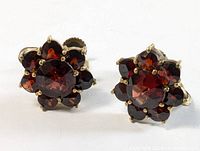 Close-up front view of the pair of vintage gold plated garnet twist-on earrings showing faceted red stones arranged in flower shape.