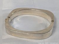 Photo of the thick, polished sterling silver bracelet showing its square oval shape and hinge clasp.