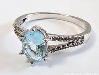 Close-up front angled view of the sterling silver blue topaz ring, showing the gemstone and band with clear stones.