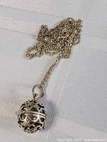 Photo of necklace chain with ball-shaped pendant resting on fabric showing chain and detailed design of pendant