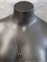 Full view of sterling silver necklace on mannequin showing 24 inch length and circular pendant with small clear stones.