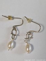 Pair of sterling silver earrings with oval white freshwater pearl drops, curved hook design with toggle and ring detail, clear plastic stoppers included.