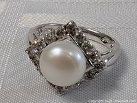 Close-up front angle of sterling silver pearl ring showing pearl and surrounding square stone frame.