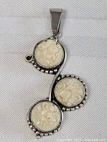 Front view of the vintage sterling silver pendant showing three carved floral ivory-colored round settings connected with a curved silver frame accented with silver beads.