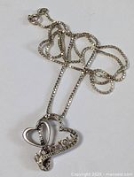 Sterling silver chain necklace laid out showing the box chain and pendant with double heart and 'I LOVE YOU' design with embedded stones.