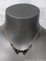 Front view of gold plated garnet necklace on gray mannequin showing chain and pendant arrangement.