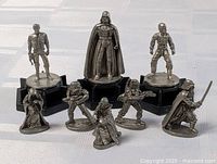 Front view of eight metal Star Wars mini figures on a white surface, three on black stands, five standing individually.