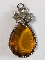 Front view of the vintage Scottish-themed pendant showing the amber-colored faceted teardrop stone set in a silver-tone twisted rope frame with a detailed thistle motif on top.