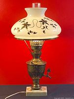 Front view of antique hurricane lamp with floral milk glass shade and brass samovar base on marble platform