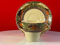 Front view of antique teacup with matching saucer, showcasing hand painted countryside design and black checkerboard border.