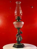 Full view of antique oil lamp showing glass chimney, pink frosted glass font with painted floral designs and metal figurine base.