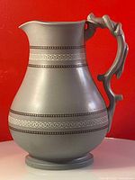 Side view showing the full pitcher with its unique sculptural vine-like handle and mosaic bands around the body.