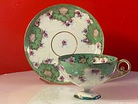 Side view of the teacup placed in front of the saucer showing hand painted floral and gold design on porcelain.