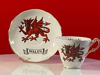 Full view of teacup positioned with matching saucer behind, clearly showing red dragon and Wales banner on both items.