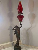 Oil lamp showing front view of the bronze finish resin statue holding the red ruby glass chimney and base.