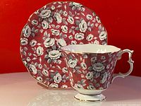 Porcelain teacup and saucer with floral rose pattern on red background, gold trim detail.
