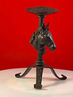 Front view of wrought iron candle holder featuring detailed horse head sculpture with chain and tripod base.