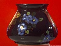 Photo of vase showing dark background with hand painted blue flowers and leaves.