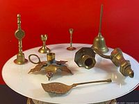 Top view of nine brass items on round white table including candle holders, bells, and a perforated ladle.