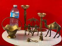 Full lot of brass decorative pieces including candle holders, basket, camel figurine, umbrella couple sculpture, and small figurines.