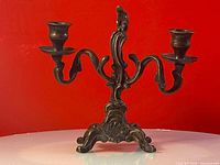 Front view of the solid brass double arm candle holder against a red background showing full structure and ornate design.