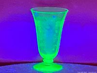 Front view of uranium glass vase glowing bright green under ultraviolet light