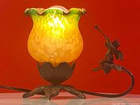 Side view of the lamp showing the glowing yellow and green hand painted glass shade and the angel figurine on the cast iron base.