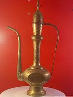 Front angled view showing the detailed etched brass surface, curved spout, bulbous body, and ornate handle.