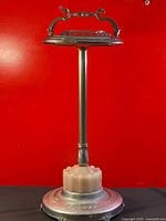 Full view of the standing ashtray showing base, stem, and top dish with handle against red background.