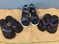 Three pairs of men's sandals and flip flops, one Skechers Massage Fit sandal and two pairs of flip flops, all black/navy with rubber soles.