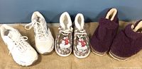 Three pairs of women's footwear on burlap background: white Brooks running shoes, snowman fleece slippers, and purple plush slippers.