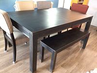 Full view of dining table surrounded by 4 chairs and a bench, showing finish and upholstery colors