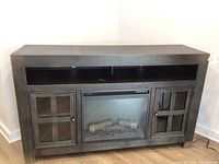 Full view of the Ashley media cabinet with electric fireplace in center and two glass door side cabinets, distressed black finish.