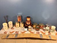 Wide shot of all assorted candles, wood candle holder, and diffuser sticks arranged on a table with leaf pattern cloth