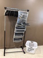 Photo showing wheeled clothes rack with felted hangers arranged on the bar, hanging shoe organizer attached to rack, and laundry basket on floor.