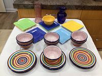 Colorful dishes with multi-colored striped plates and bowls, square dish plates in solid pastel colors, and two decorative vases on a kitchen counter.