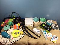 Photo showing assorted dog toys including rubber hippo, tennis ball, rope toys, and several leashes, bowls and boxed grooming items