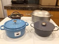 Four pots: blue Staub, gray Cooks Essentials, small brown saucepan, aluminum roaster