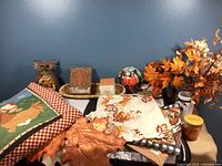 View of all fall decor items arranged on a surface including fabrics, faux leaves, owl figurine, candles and small decor