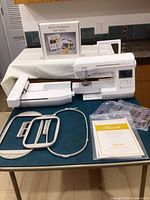 Baby Lock Flourish sewing and embroidery machine on table with embroidery arm attached and Embroidery Start-Up Kit box behind