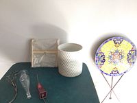 Photo showing all items together on a table, including folded framed art, ceramic planter, round mosaic patio table, metal branch art, glass vase and glass chime.