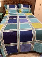 Full view of bed with woven rattan headboard, patterned multi-color quilt, and shams.