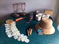 Full lot overview showing hummingbird feeders, ceramic planters, chime, gardening tools, hat, and pruning shears on a green table