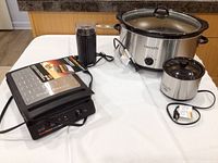 Kitchen countertop with all items: Chef's Choice waffle maker, two Crockpots, Haridor grinder