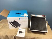 Med Massager therapeutic foot massager device displayed alongside its box and owner's manual on a burlap surface.