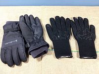 Two pairs of black men’s winter gloves displayed side by side. Left pair is Carhartt, insulated, with wrist straps and synthetic leather palms. Right pair is heavy knit fabric with rubber grips.
