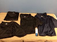 Two black 32 Cool short sleeve collared shirts and one navy 32 Cool shirt shown folded on a brown blanket.