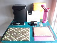 Photo of office supplies including AmazonBasics paper shredder, unopened yellow envelopes, pink binder, pink OttLite desk lamp, fabric pinboard, and accessories on a table.